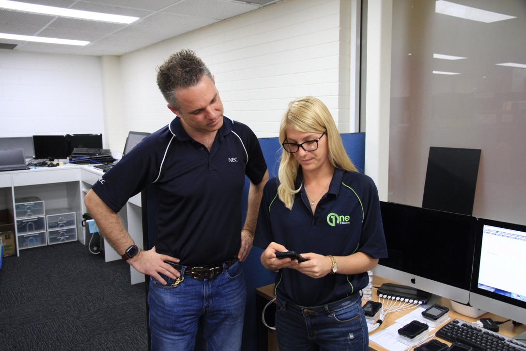 Benjamin Smith and a One IT Services team member reviewing a handheld device beside computer workstations.
